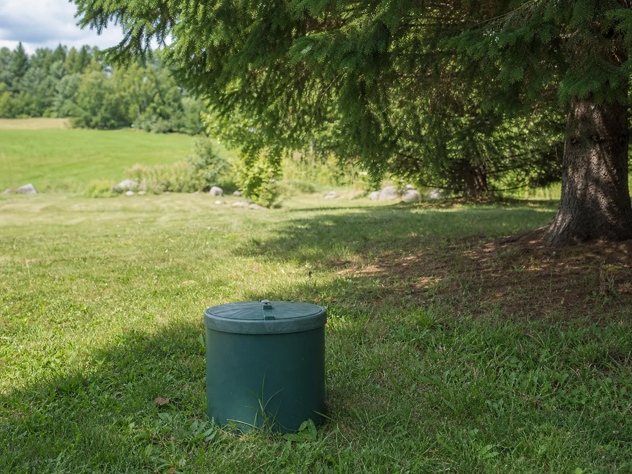 rural-new-hampshire-backyard-well-casing-cap-in-green-lawn-beside-pine-trees-natural-daylight-clean-editorial